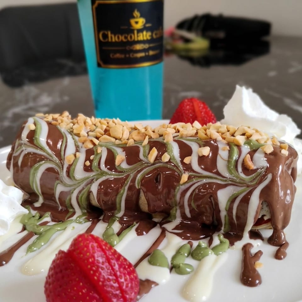 Chocolate-covered dessert topped with chopped nuts, green and white drizzle, strawberries, and whipped cream on a white plate.