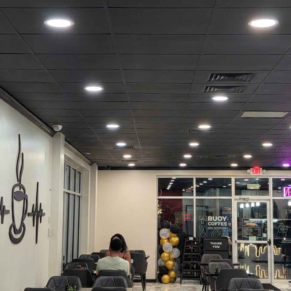 Modern coffee shop interior with lounge seating, patrons, balloon columns, coffee signage, and a neon welcome sign.